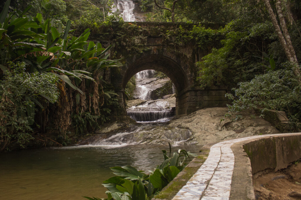 Stone bridge and waterfall along a forest trail at Tijuca National Park in Rio de Janeiro, Brazil, surrounded by lush tropical vegetation.