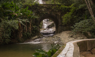 Stone bridge and waterfall along a forest trail at Tijuca National Park in Rio de Janeiro, Brazil, surrounded by lush tropical vegetation.