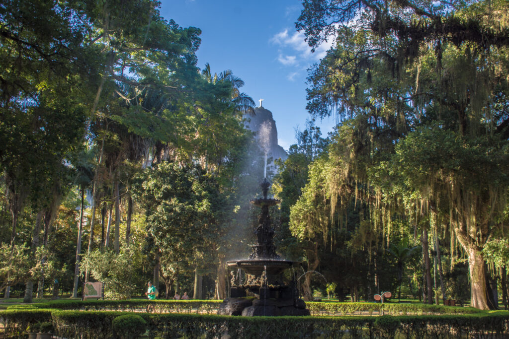 Ornate fountain at the Botanical Garden of Rio de Janeiro, Brazil, surrounded by lush tropical trees with the Christ the Redeemer statue visible in the background.