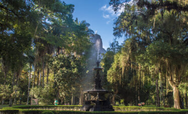 Ornate fountain at the Botanical Garden of Rio de Janeiro, Brazil, surrounded by lush tropical trees with the Christ the Redeemer statue visible in the background.